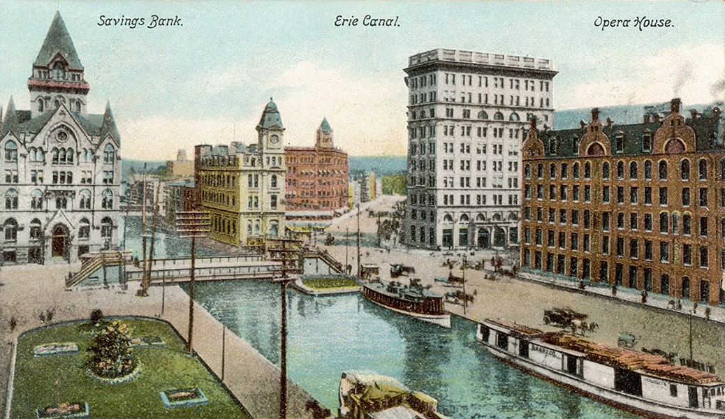 A colorful illustrated image of Erie Canal with three boats docked; to the left of the canal is a large building depicting the savings bank, and on the right, the opera house