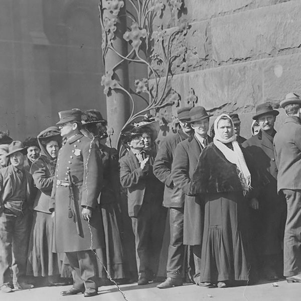 A black-and-white photograph of people waiting outside a bank in a line alongside police officers.