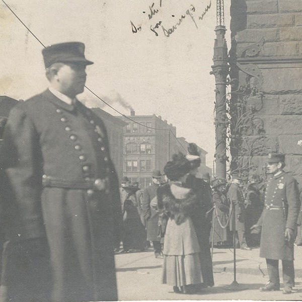 A black-and-white photograph with a police officer in the foreground and people waiting in line outside the bank.