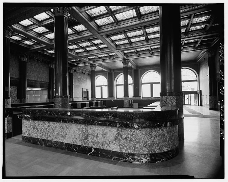 A black-and-white photograph of the inside of an empty banking lobby with an empty booth in the foreground.