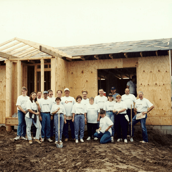 A colored photograph of KeyBank volunteers standing in front of a house that's under construction.