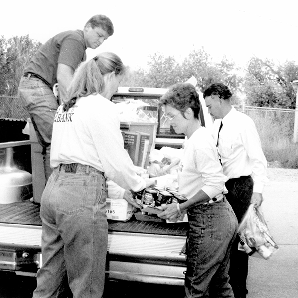 A black-and-white image of volunteers taking food out of the back of a pickup truck.