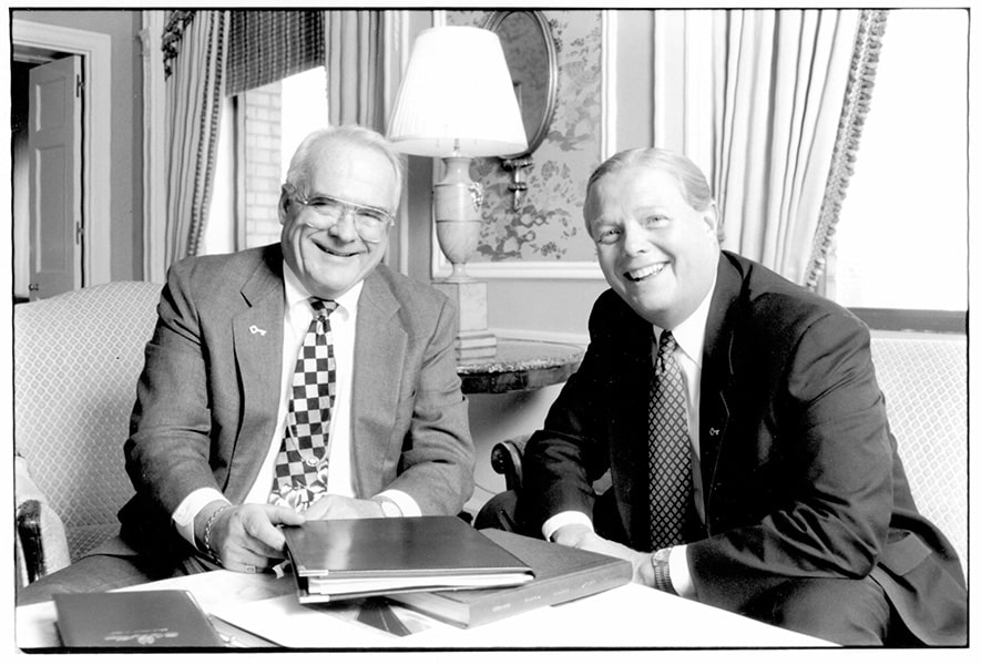 A black-and-white image of Victor J. Riley Jr. and Robert Gillespie sitting behind a desk with a stack of reports.